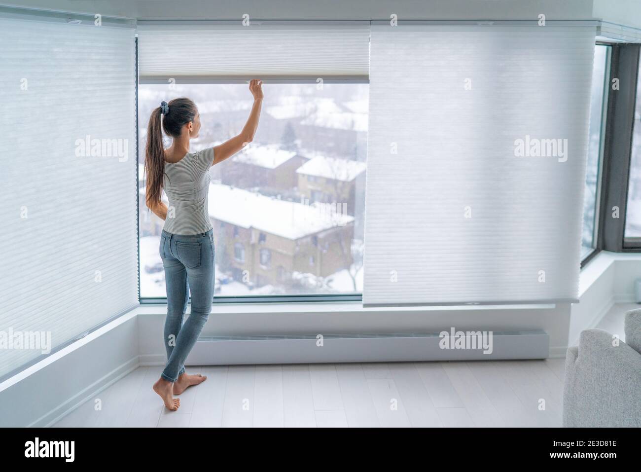 Woman closing cellular shades on apartment window keeping energy and heat indoors with honeycomb blind curtain. Cordless pleated shades in modern home Stock Photo