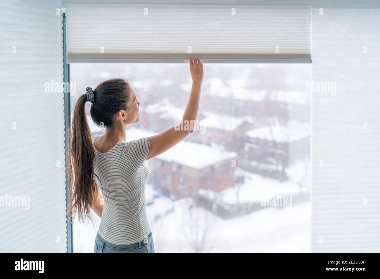 Home blinds window shades woman opening shade blind during winter morning. Asian girl holding modern cordless top down luxury curtains indoors Stock Photo