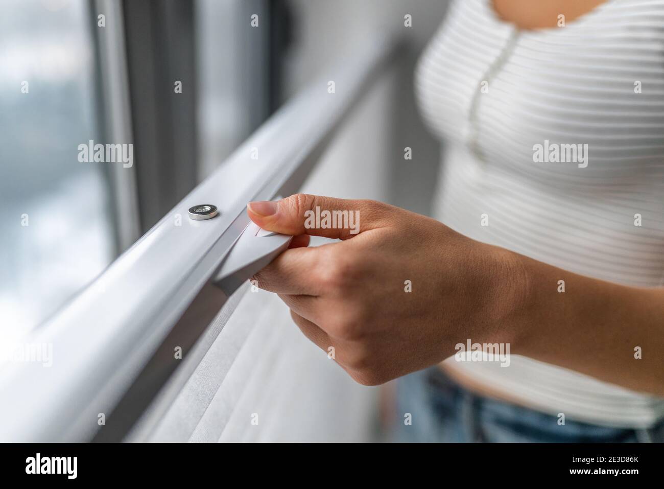 TOP-DOWN BOTTOM-UP WINDOW SHADES. Woman raising shade blind at home from the lower to the top of windows Stock Photo