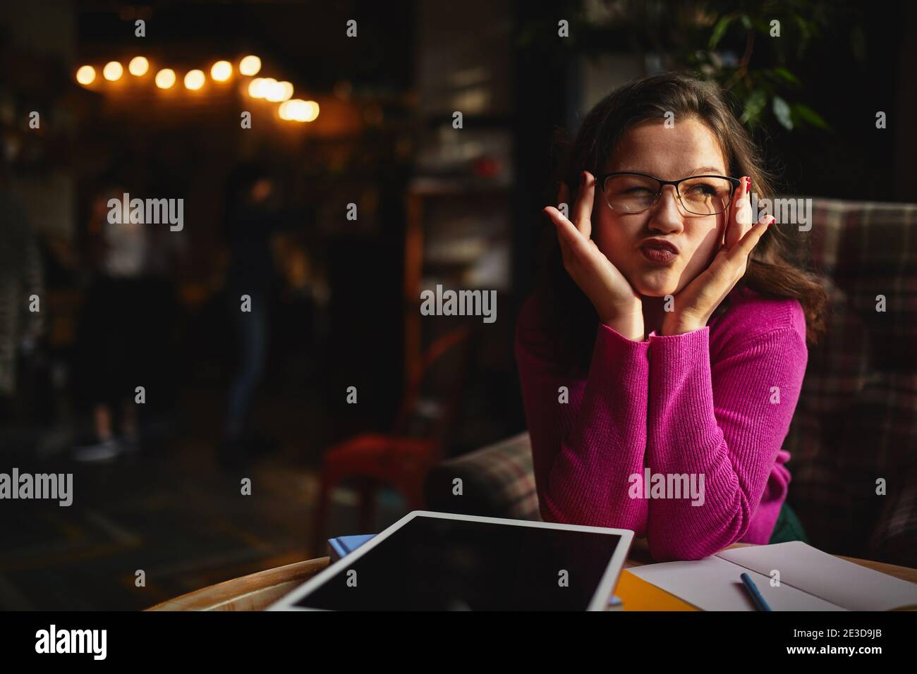 Young female making grimace while sitting in coffee house and working with digital tablet Stock Photo