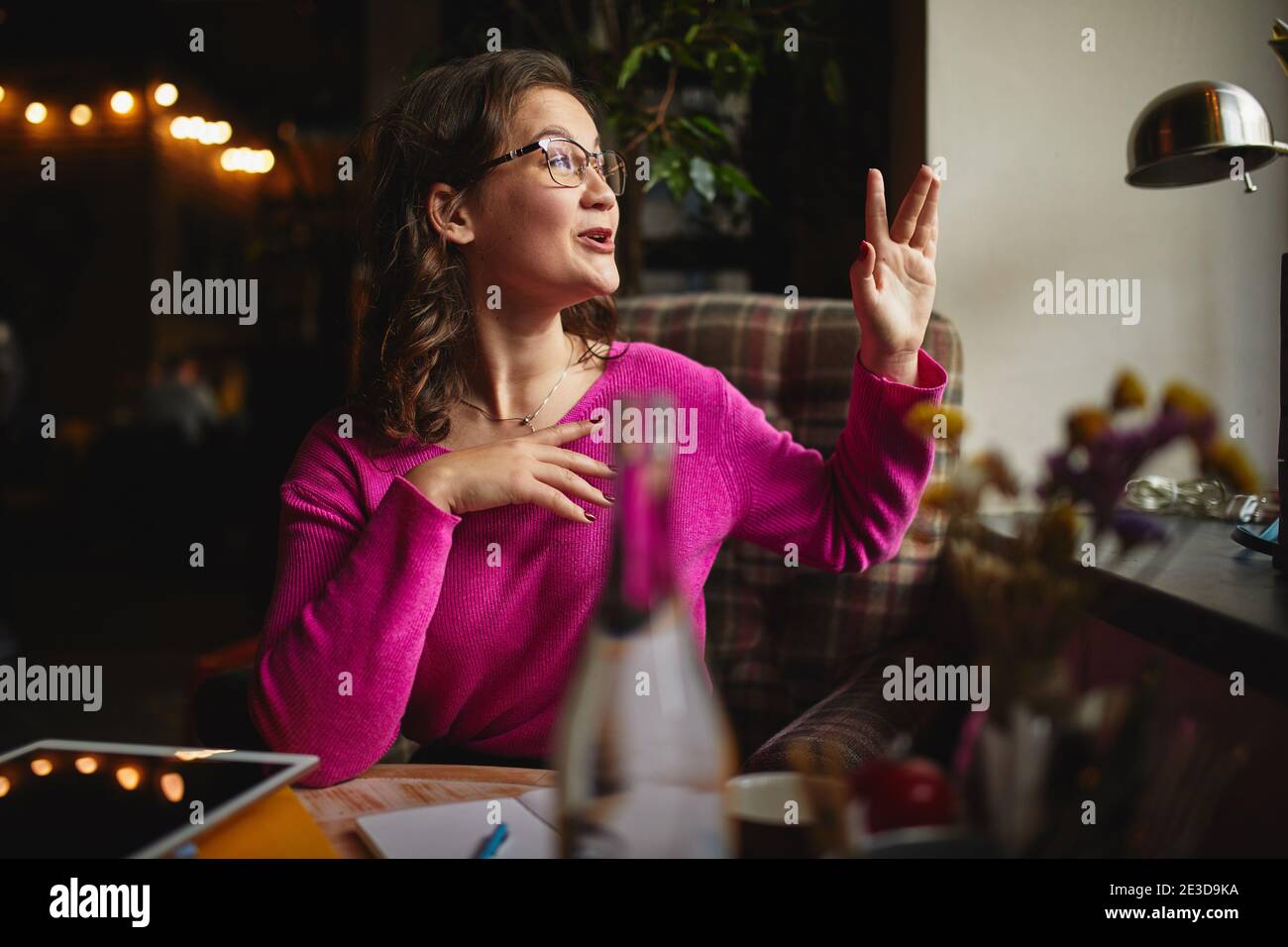 Young pretty woman resting in coffee house while waving to her friend outside Stock Photo