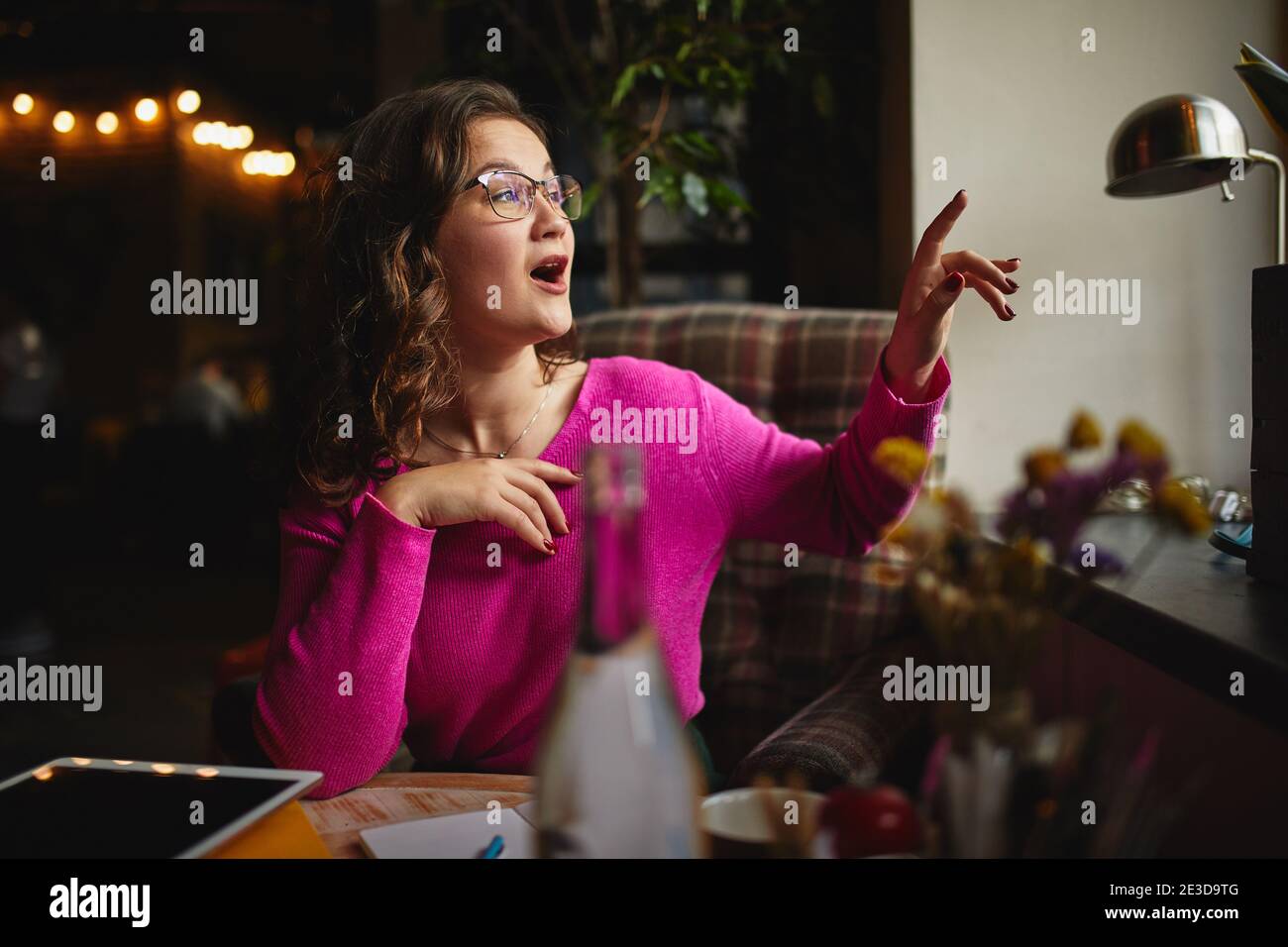 Attractive young lady wearing glasses and working indoors while waving to her friend outside the window Stock Photo