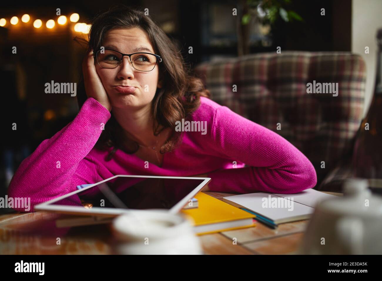 Portrait of young woman working in coffee house while leaning face on hand and making grimace Stock Photo