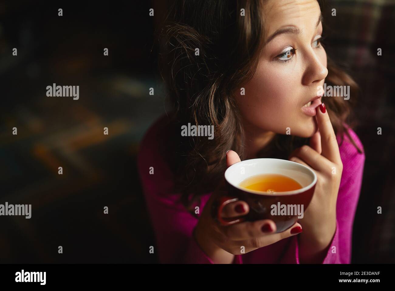 Close up of attractive lady touching lips and holding red cup of tea in coffee house Stock Photo