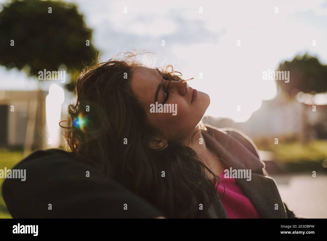 Happy pretty lady with closed eyes sitting in the park and having rest in the sun Stock Photo