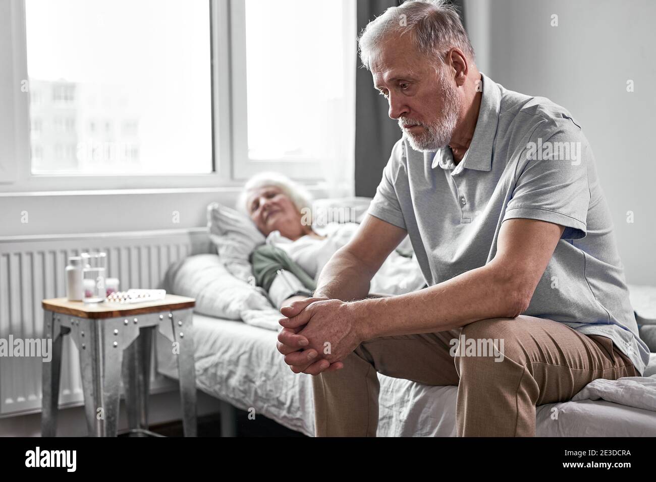 upset pensioner man sits in depression while her sick woman suffering from covid-19, he wants wife to be healthy Stock Photo