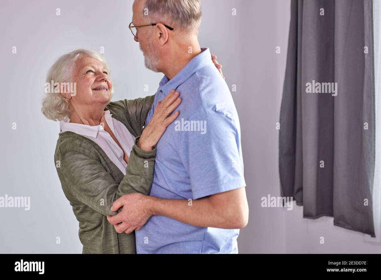 senior couple dancing in living room, husband holding hand of mature wife enjoying fun together, spend holidays, leisure retirement ifestyle at home. Stock Photo