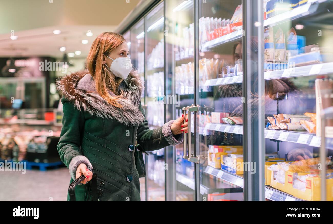 Woman at supermarket freezer section wearing face mask Stock Photo
