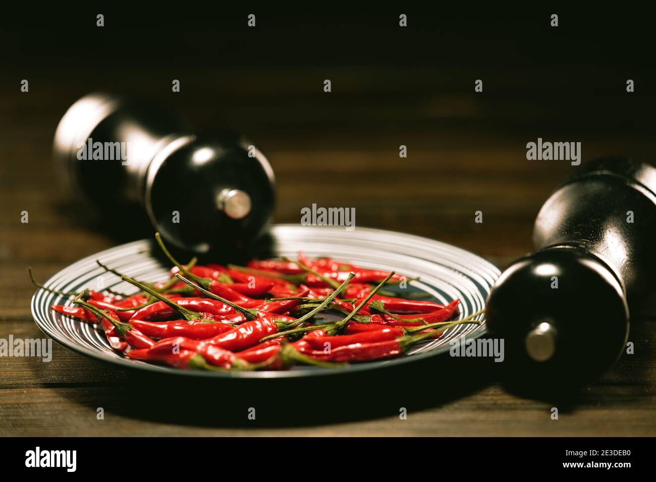 Fresh Red Birds Eye Chilli in a plate on a wooden table with a BLACK SALT and PEPPER GRINDER SET Stock Photo