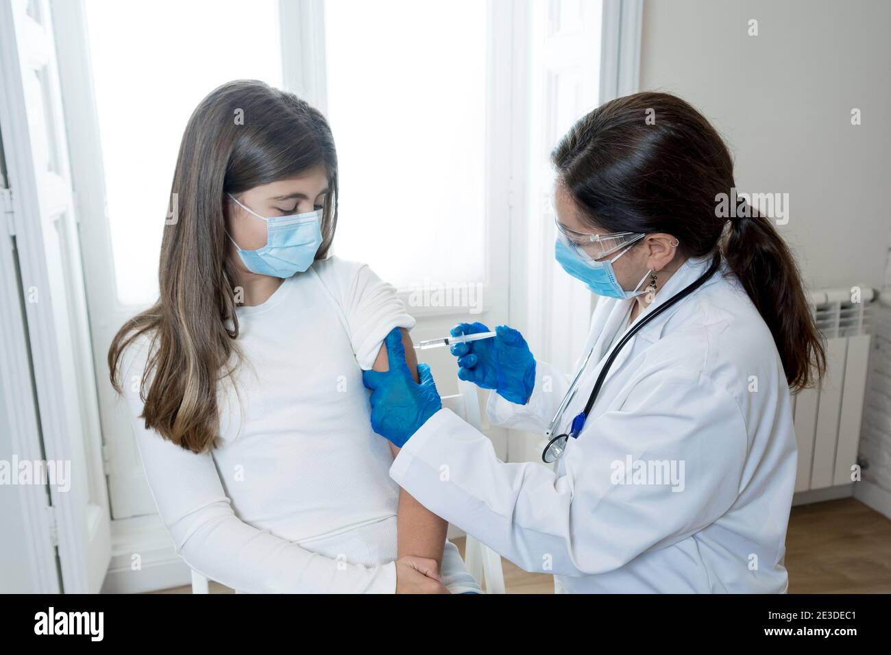 Nurse administering the coronavirus vaccine to a a young girl patient with face mask in Doctors clinic. Immunization, medical treatment and Covid-19 v Stock Photo