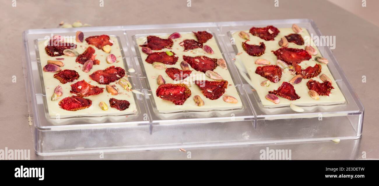 Three white chocolate bars with strawberry chips. They are in plastic form on a metal surface. Close-up. Stock Photo