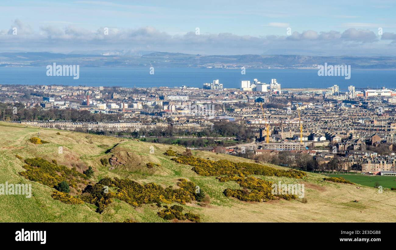 Sun shines on the slopes of Arthur's Seat, with the Edinburgh neighbourhoods of Leith and Lochend behind, and Fife across the Firth of Forth in the di Stock Photo