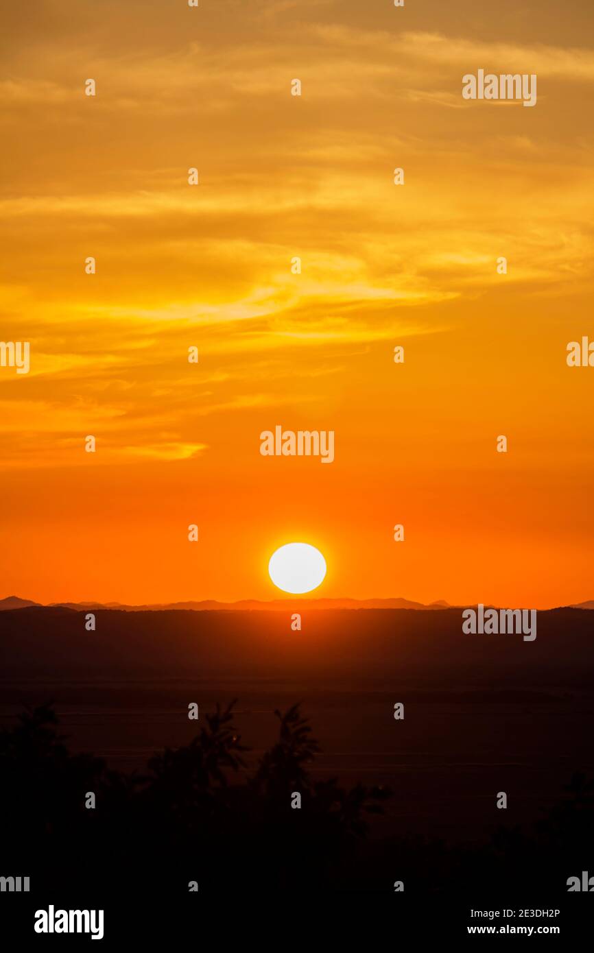 A landscape of the golden sky, the silhouetted earth and the setting sun Stock Photo