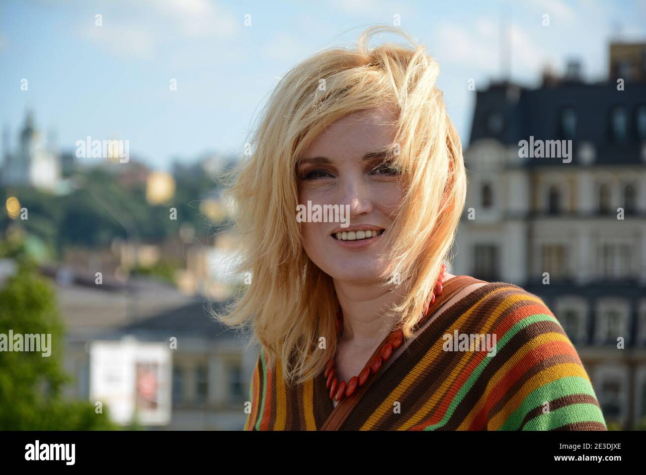 A woman with 1970-style hairstyle and clothes smiles outdoors Stock Photo