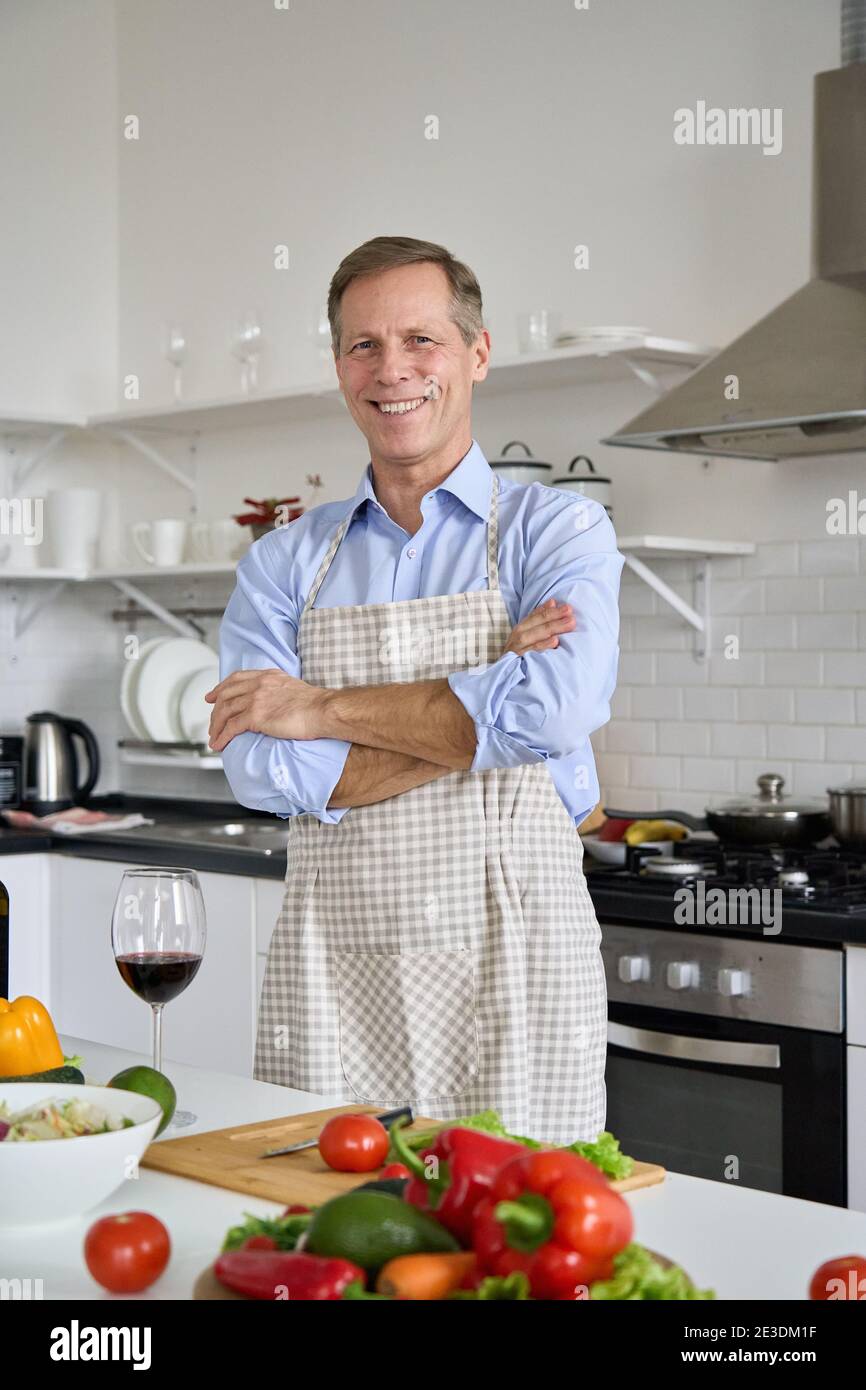 Happy middle aged man wearing apron cooking salad at home, portrait. Stock Photo