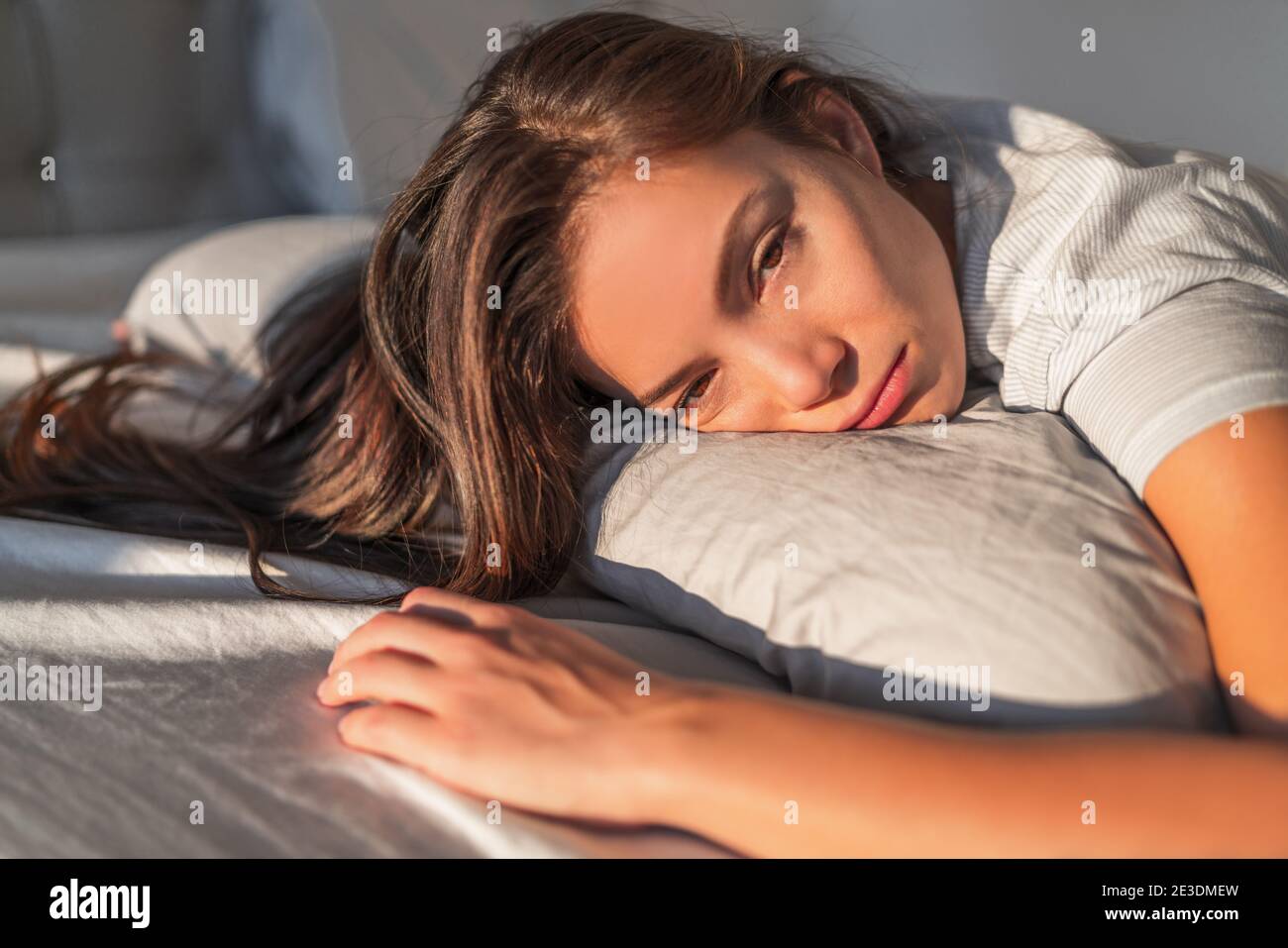 Funny tired lazy asian young woman waking up in bed sleepy morning