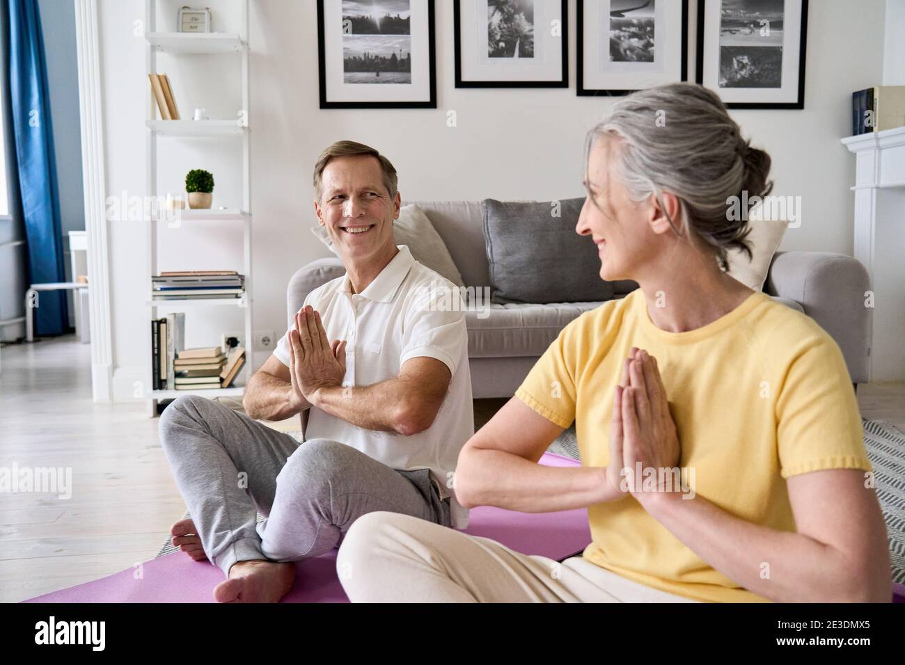Happy healthy older senior 50s couple meditating with namaste hands at home. Stock Photo