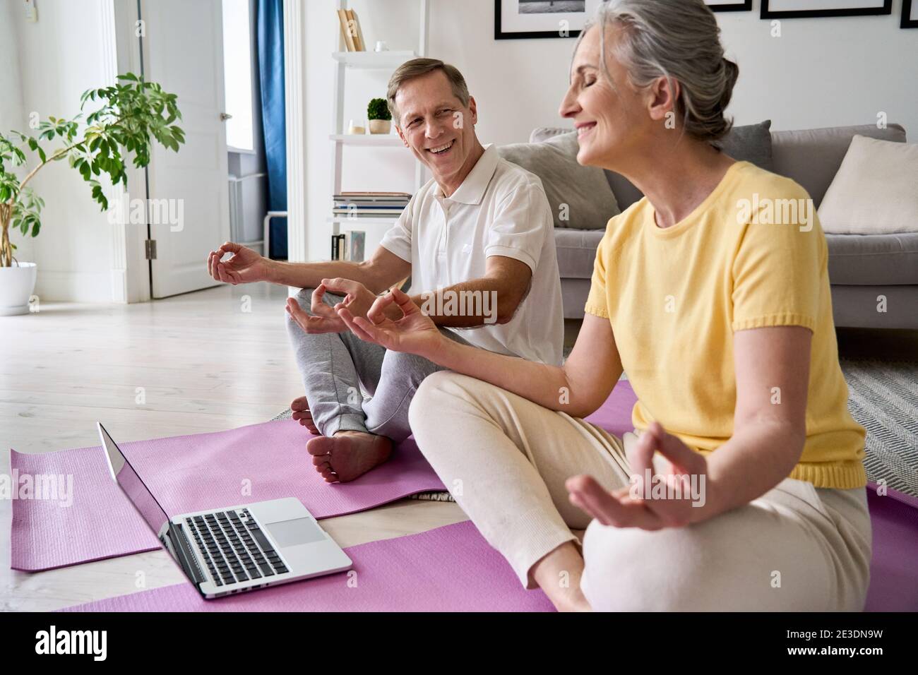 Happy senior couple having fun learning to meditate, watching online yoga class. Stock Photo