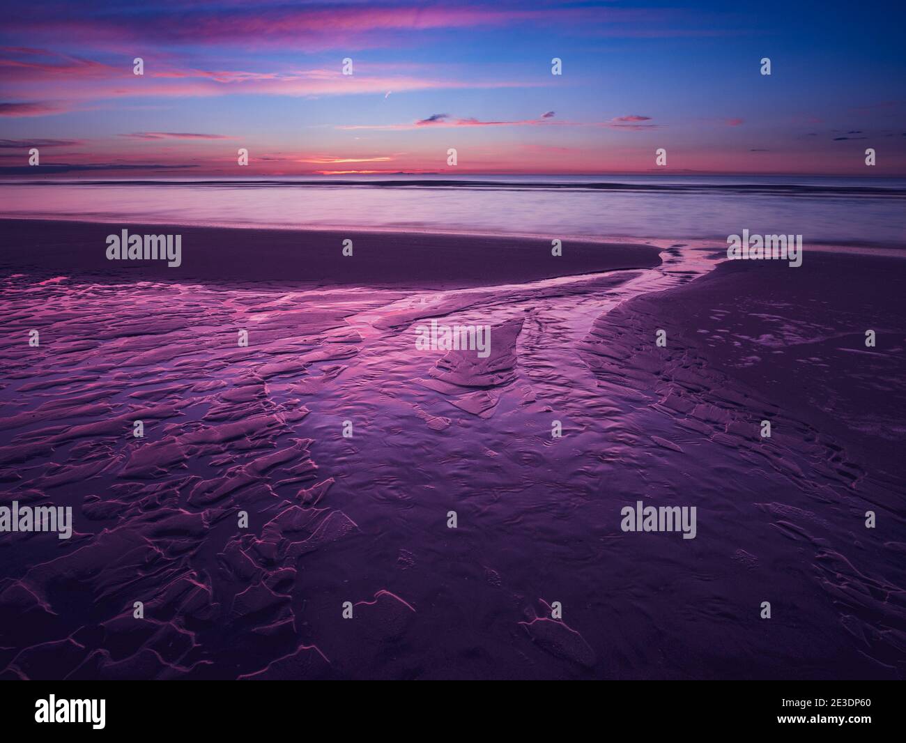 Colorful purple sunset at the beach with sand ripples in the foreground at low tide Stock Photo