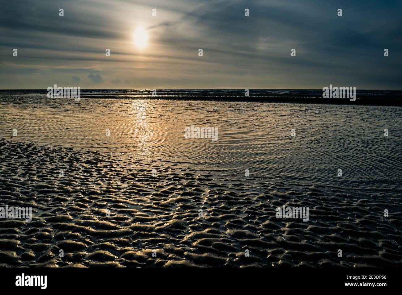 Setting sun behind sandbank at low tide at the beach Stock Photo
