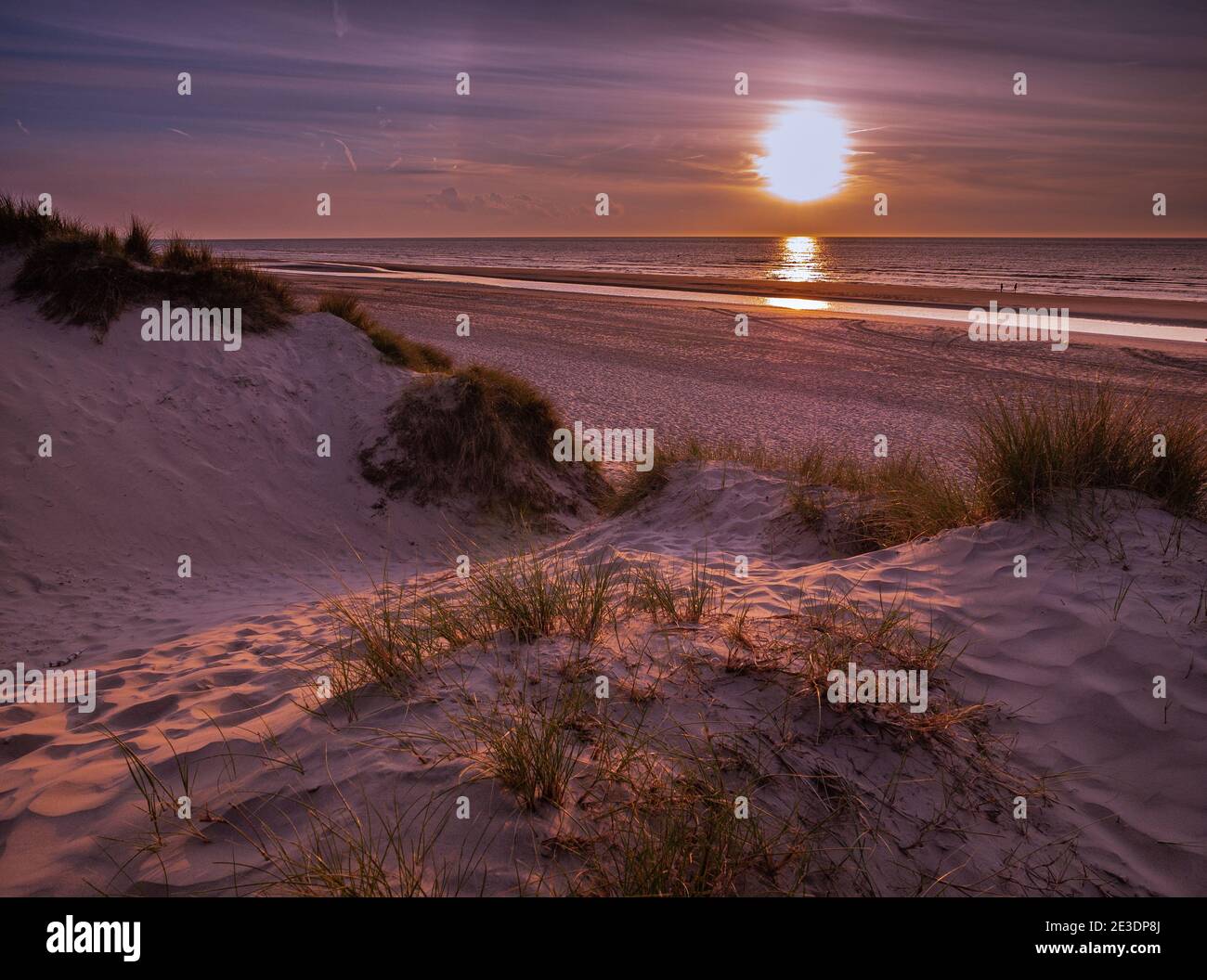 View from marram grass covered dunes towards the beach prior to a colorful sunset Stock Photo