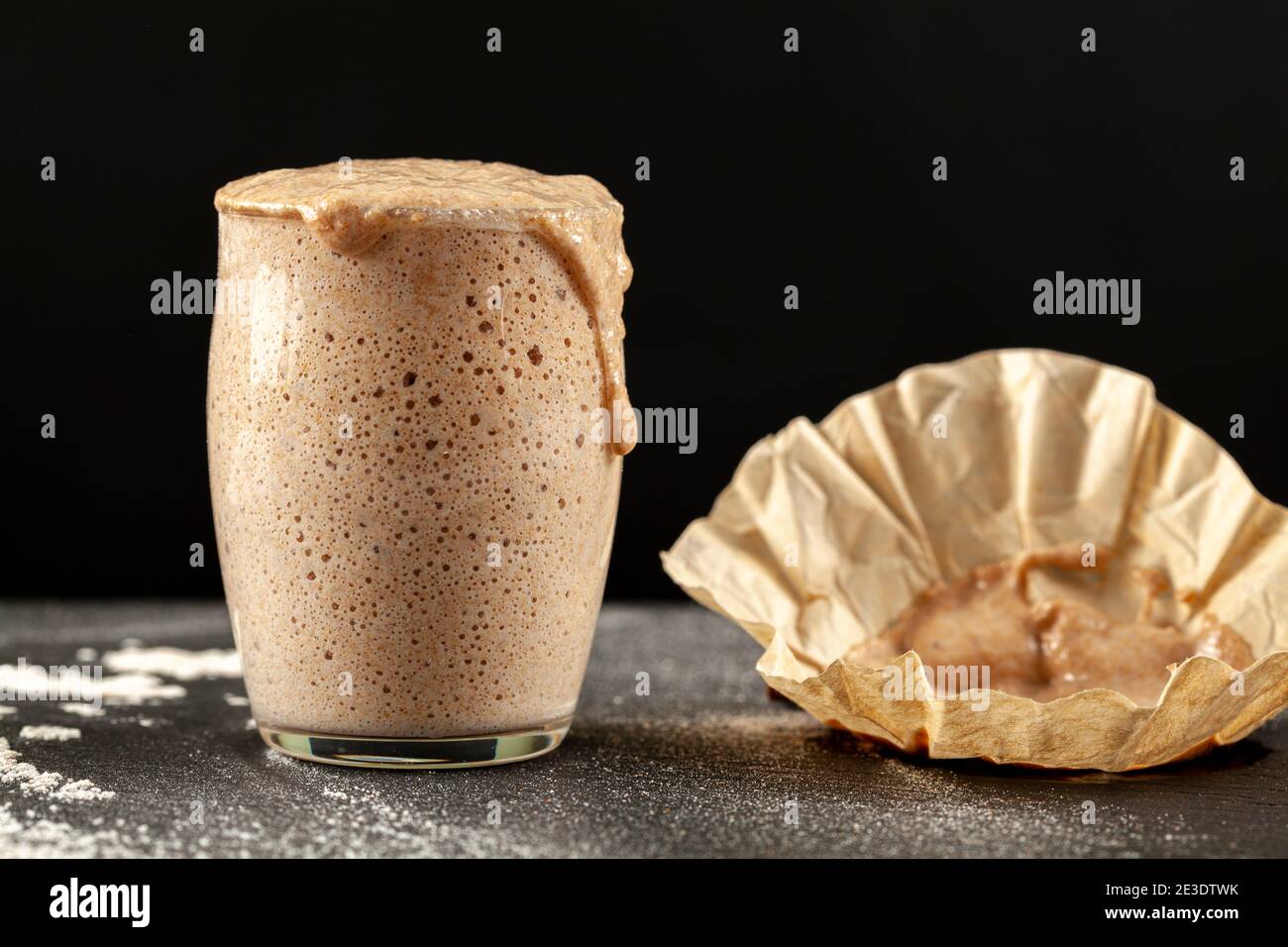 Side view of an actively rising sourdough starter culture which is overflowing over the top of the glass cup it is in. Bubbles show fermentation. The Stock Photo