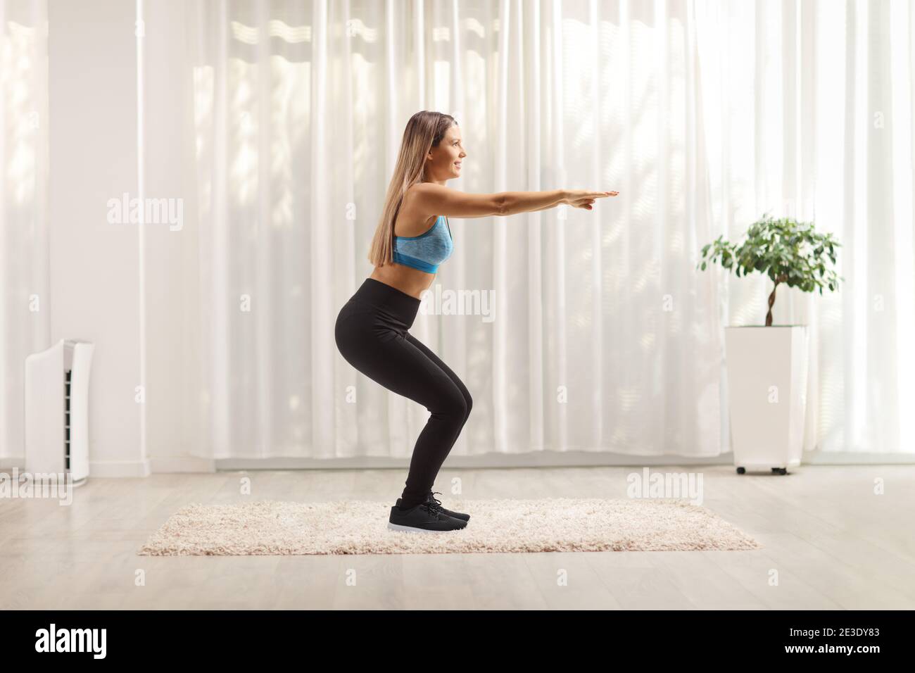 Full length profile shot of a young woman in sportswear doing squat exercises at home Stock Photo