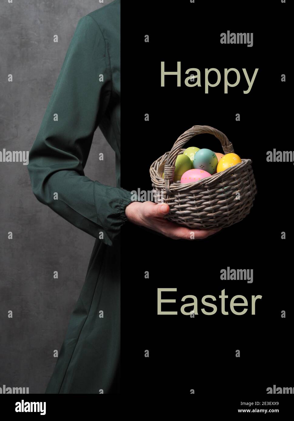 Female hand in dark green dress holding basket with colored decorative easter eggs in front of black wall with text: Happy Easter. Copy space.  Stock Photo