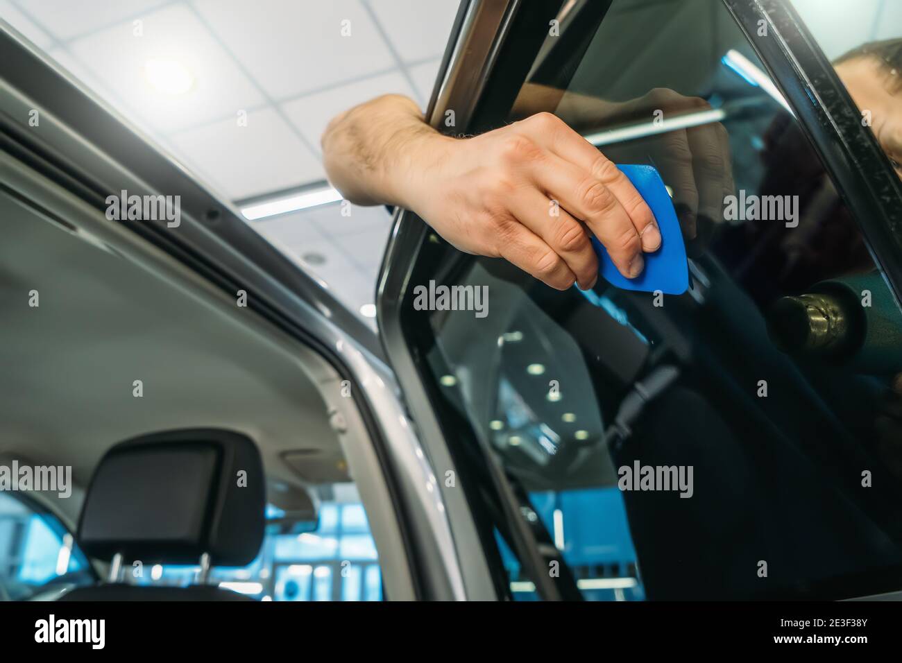 Car window tinting. Process of Installation window tint in Car Detailing Studio Garage by professional detailer. Stock Photo