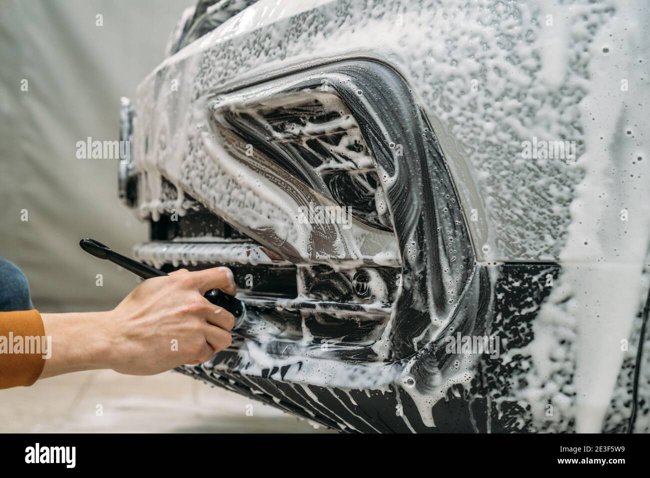 Detailed vehicle cleaning at car wash. Worker cleans bumper with foam