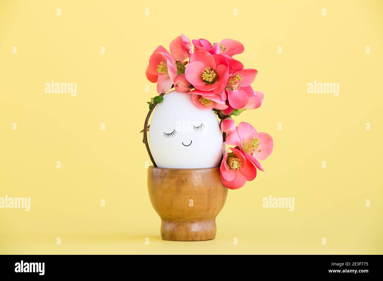 Cute egg with a painted face and spring flowers on a yellow background. Creative concept for Easter Stock Photo