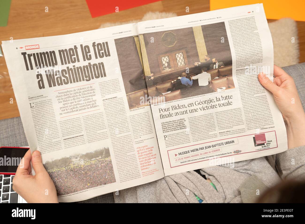Paris, France - Jan 7, 2020: Woman reading on couch French newspaper Liberation interiour page show storming of the U.S. Capitol by supporters of U.S. President Donald Trump on January 07, 2021 Stock Photo