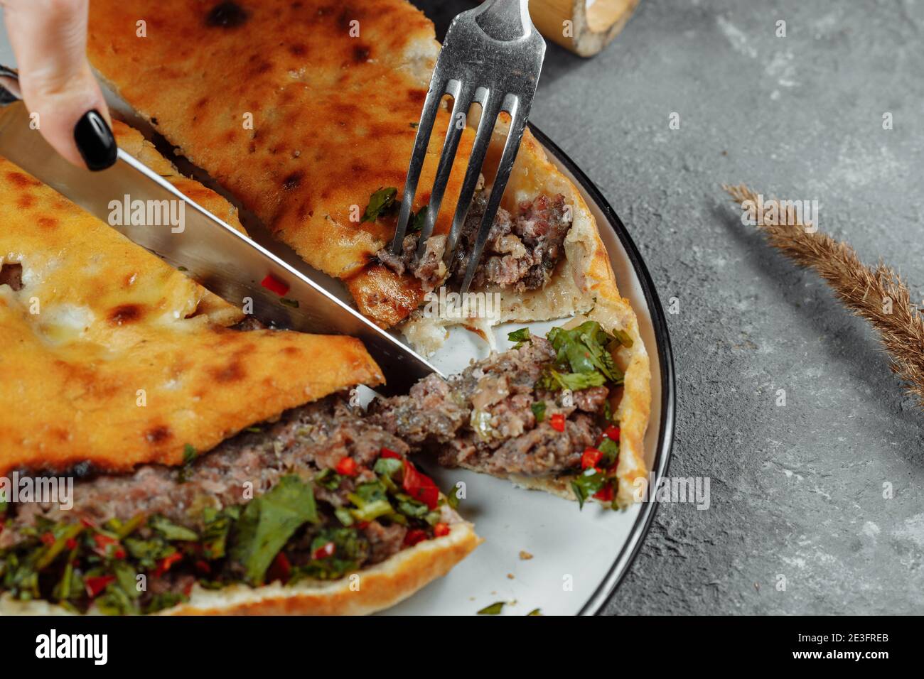 female hands with a knife and a fork cut Khachapuri with lamb and chili. Georgian national food Stock Photo