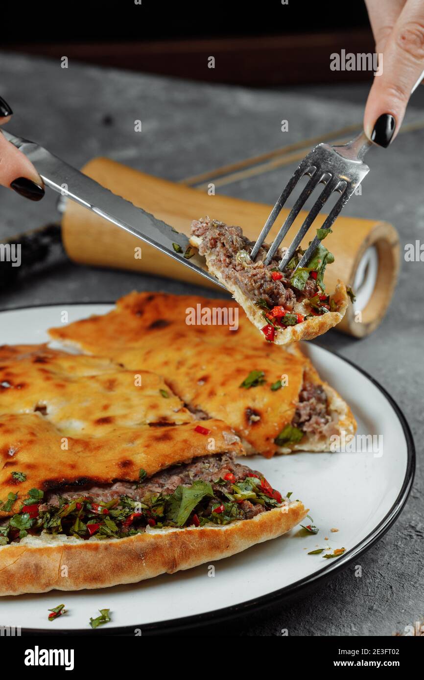 female hands with a knife and a fork cut Khachapuri with lamb and chili. Georgian national food Stock Photo