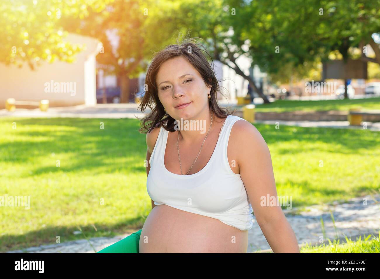 Close up of pregnant belly in nature sitting outdoors on a green grass meadow in a city park on a sunny day Stock Photo