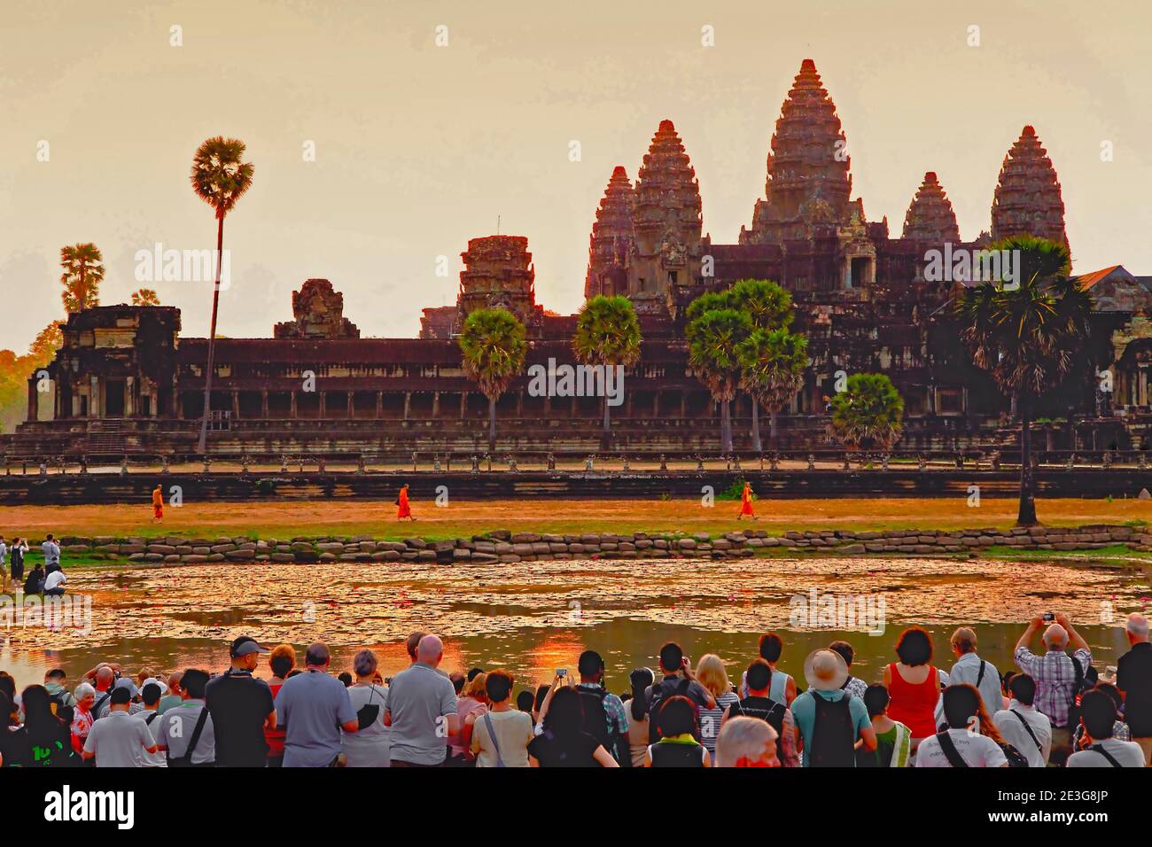 Tourists wait for the daily 'Sun up' delight at ANGKOR WAT, Siem Reap, Cambodia as three Buddhist monks walk to prayers. Stock Photo