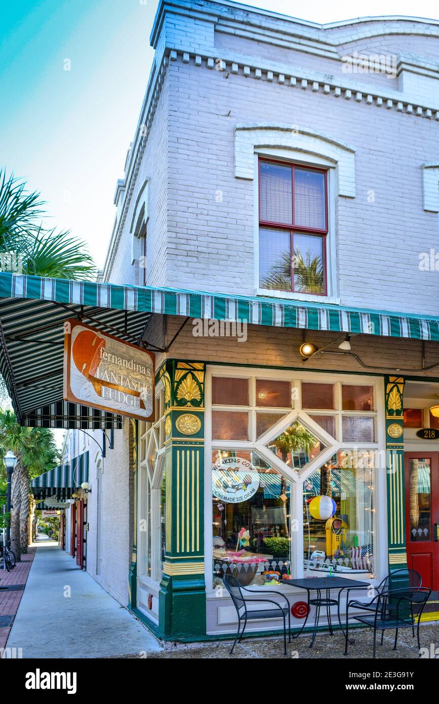 View down long palm tree lined sidewalk along side Fernandina's Fantastic Fudge sweet shop in charming old building in Fernandina Beach, on Amelia Isl Stock Photo