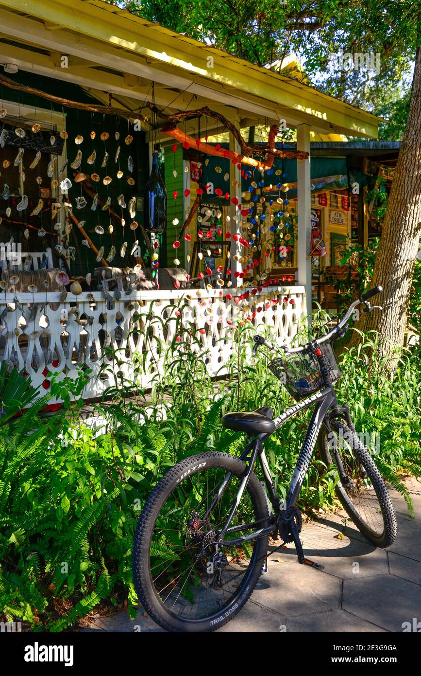 A black trail bicycle parked in front of an  old Florida style cottage with colorful seashell wind-chimes hanging all around the  front porch in downt Stock Photo