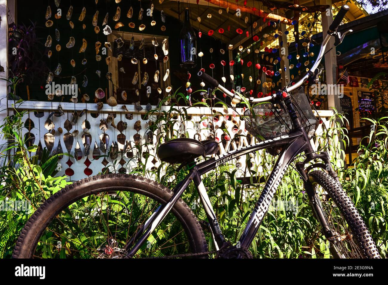 A close up of a black trail bicycle parked in front of an  old Florida style cottage with colorful seashell wind-chimes hanging all around the  front Stock Photo