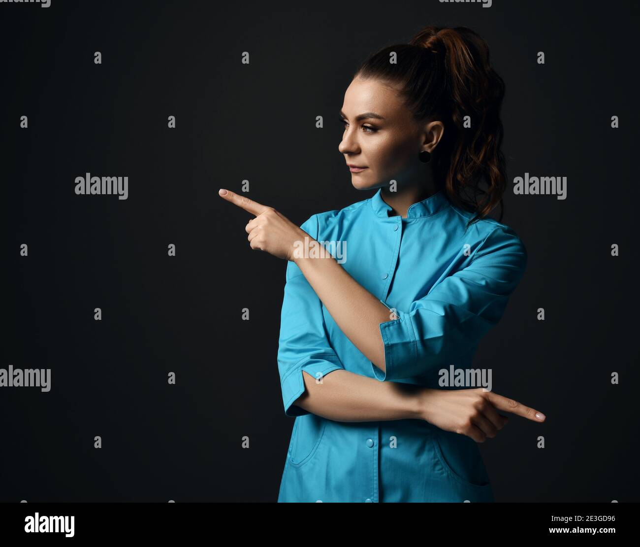 Young brunette woman doctor nurse in blue medical gown points with ...