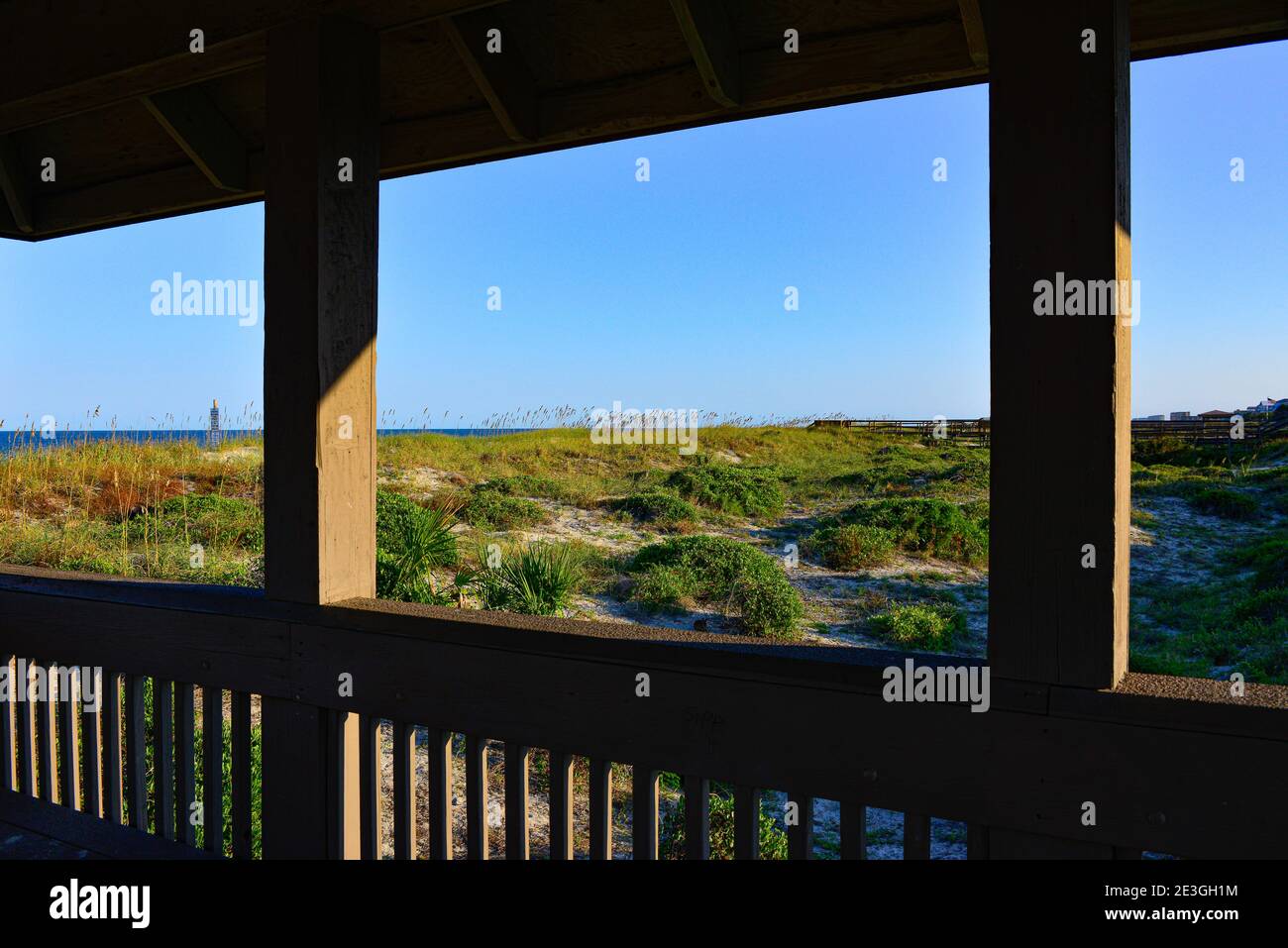View of distant water beyond the grassy dunes from wooden, covered boardwalk to the Main Beach, at  Fernandina Beach, on Amelia Island, FL, USA Stock Photo