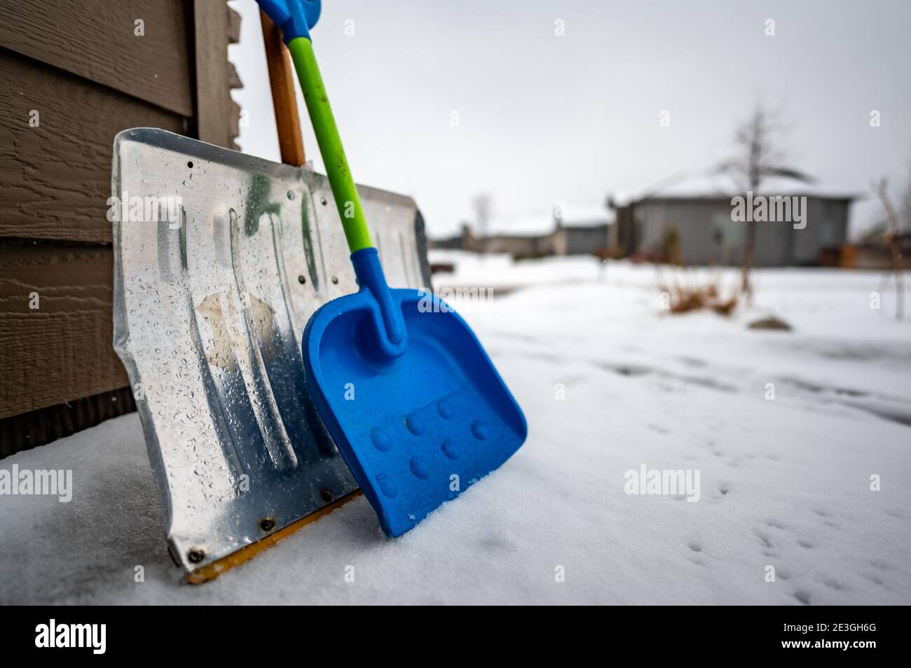 Adult metal shovel and child toy plastic shovel to imply working together to clear snow Stock Photo