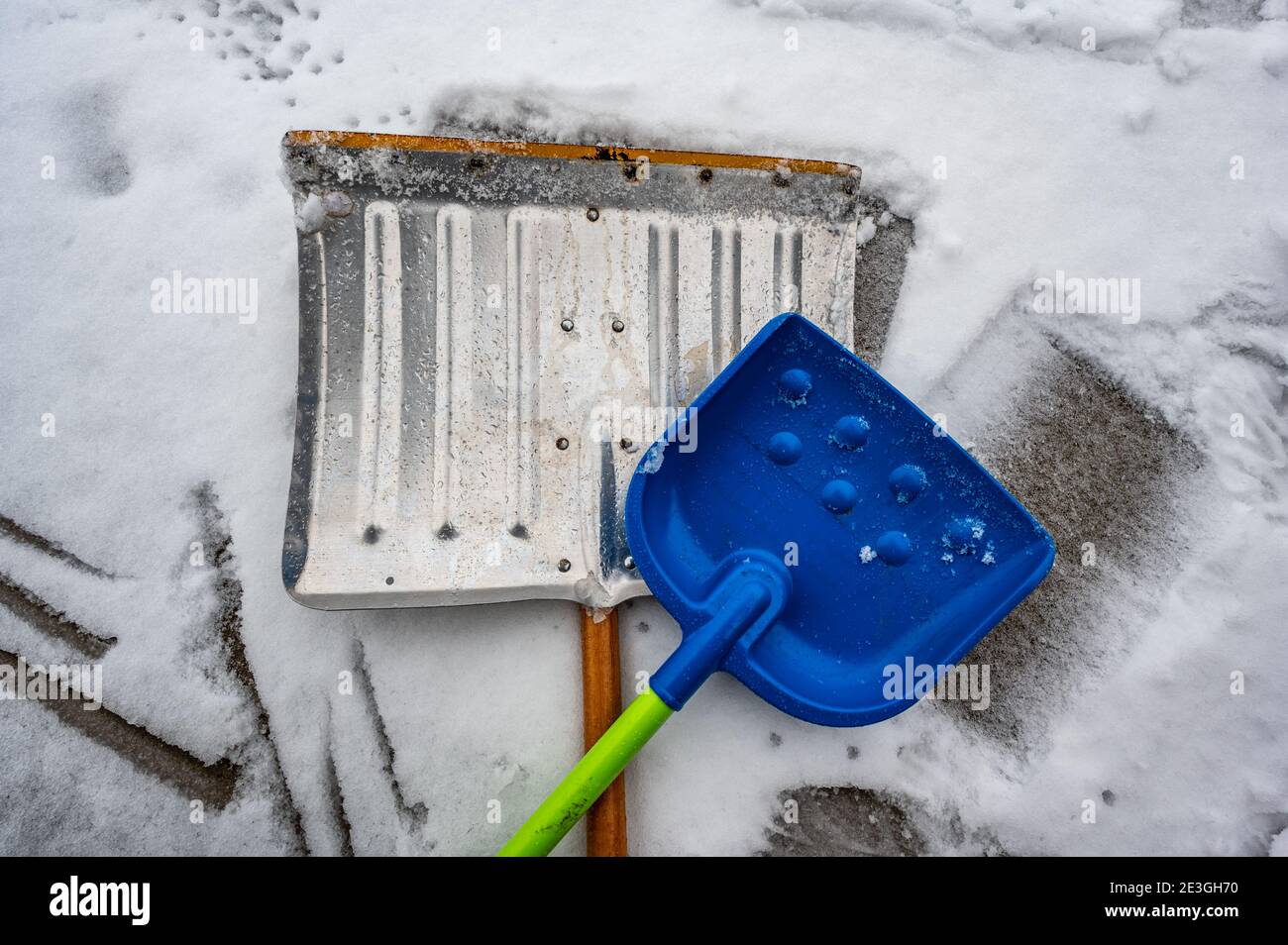 Adult metal shovel and child toy plastic shovel to imply working together to clear snow Stock Photo