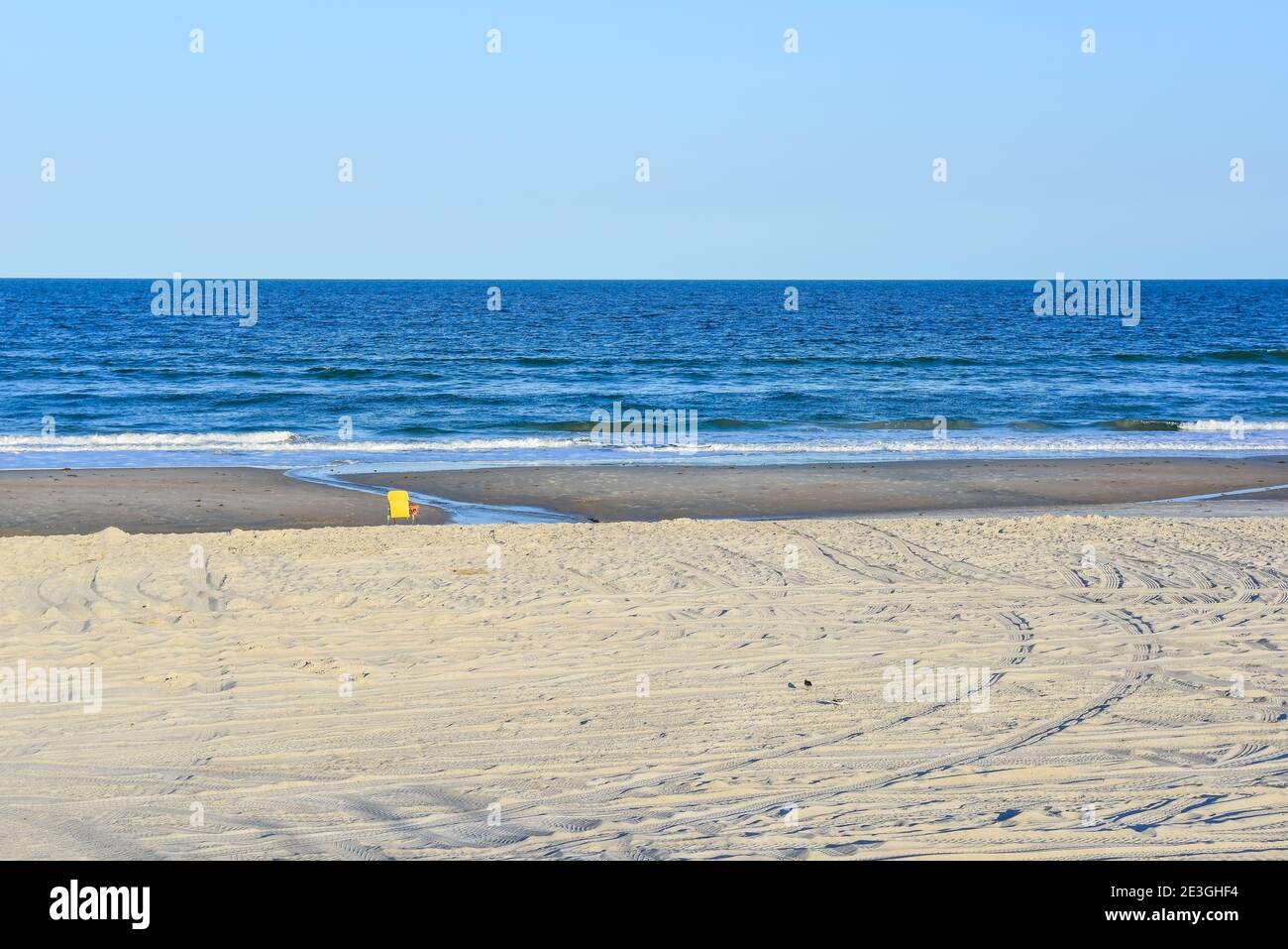 In a stark, empty beach scene, a lone yellow beach chair faces the Atlantic Ocean on Fernandina Beach, on Amelia Island, FL, USA Stock Photo