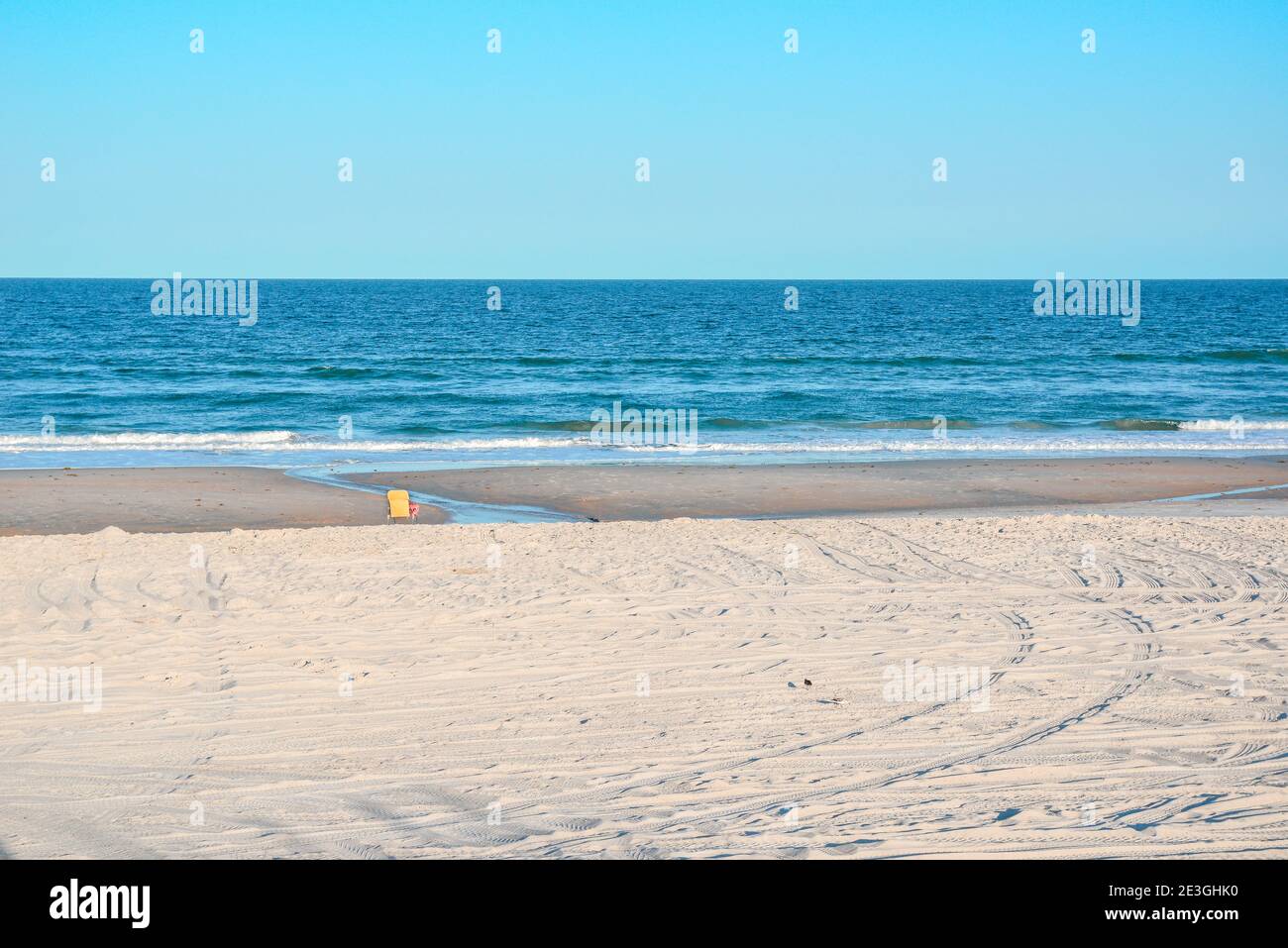 In a stark, empty beach scene, a lone yellow beach chair faces the Atlantic Ocean on Fernandina Beach, on Amelia Island, FL, USA Stock Photo