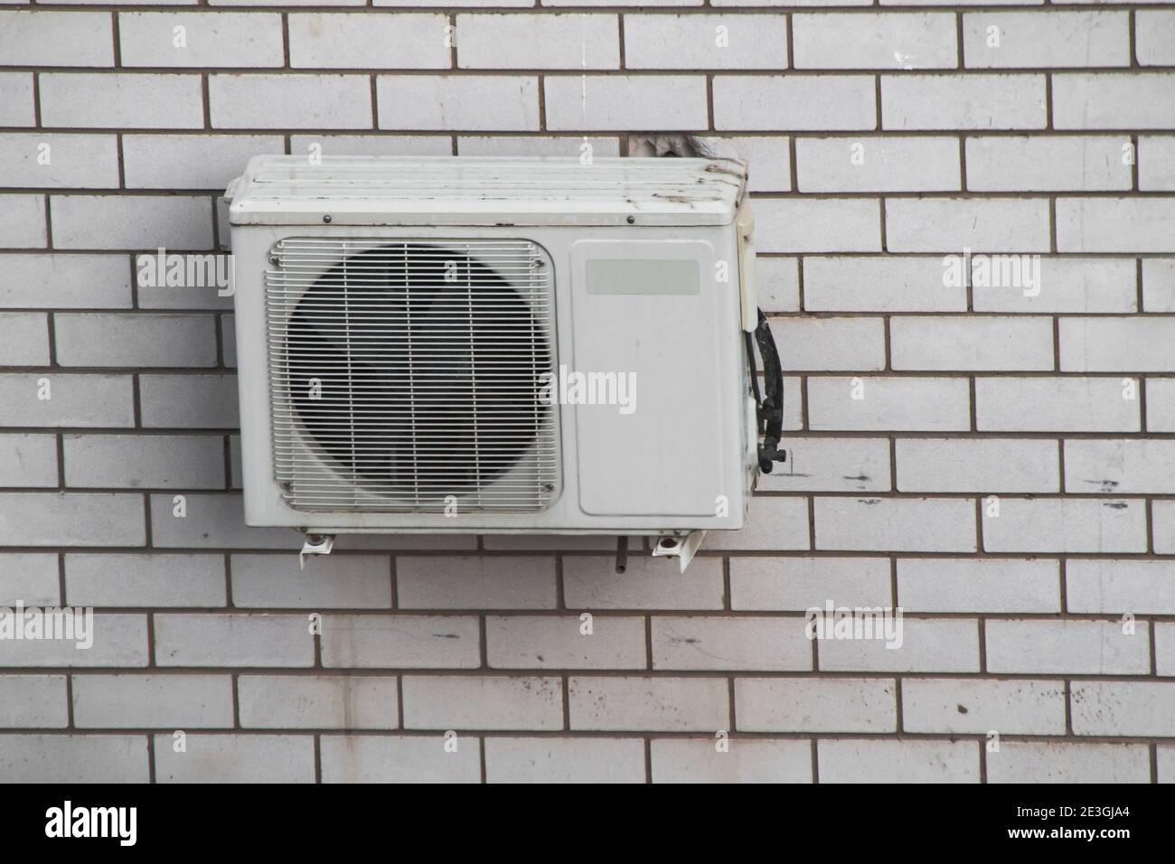 Air conditioning compressor unit on a white brick wall. Front view