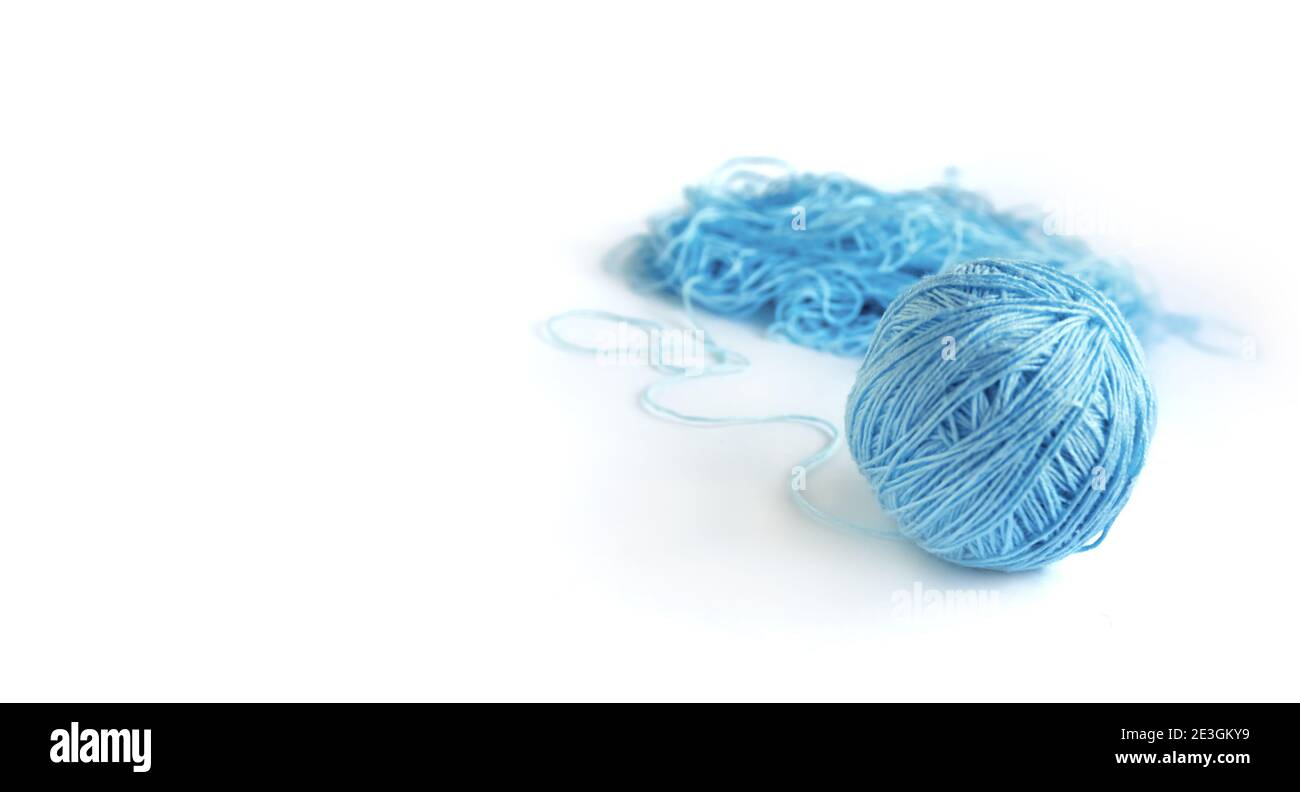 A ball of blue fine cotton yarn in the process of winding, isolated on the white background. Tangled yarn in the background. Banner, space for text. Stock Photo