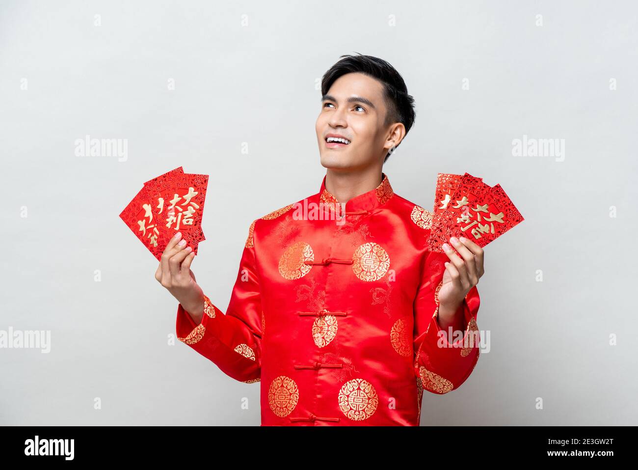 Asian man in traditional oriental costume holding red envelopes or Ang Poa with text mean lucky - wealthy for Chinese new year concepts Stock Photo