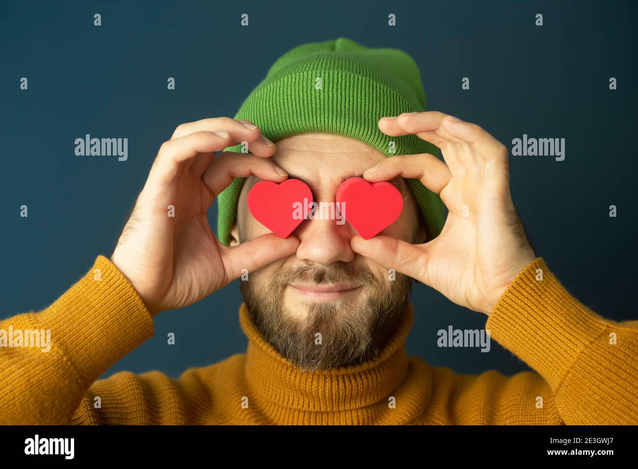 Portrait of a cheerful funny young hipster man with hearts in his eyes on a blue background. Sales, discounts, Valentine's Day and love concept. Stock Photo