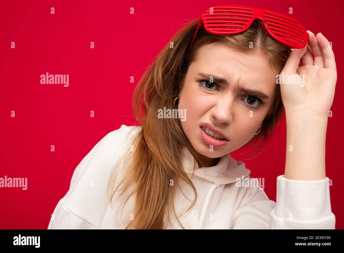 Photo shot of beautiful dissatisfied young blonde woman wearing casual clothes and stylish optical glasses isolated over colorful background wall Stock Photo